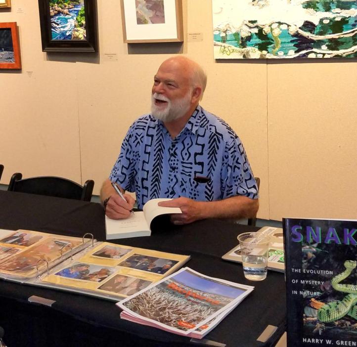 Smiling Harry Greene signs his books at a table